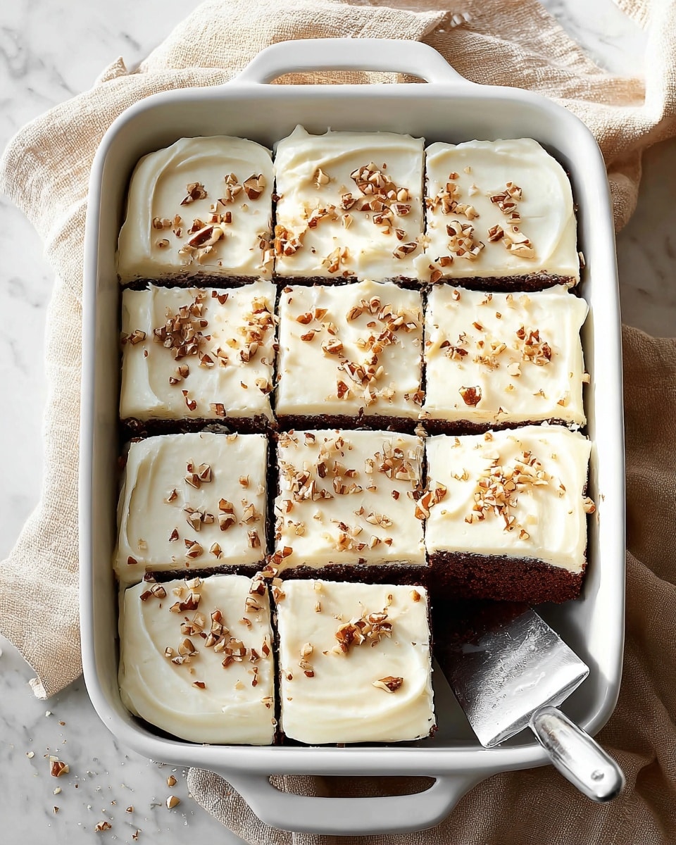A white ceramic rectangular baking dish holds a dark brown cake topped with a thick layer of smooth, creamy white frosting. This frosting layer is spread evenly and is sprinkled with small pieces of chopped nuts, adding texture and contrast. The cake is already sliced into 12 square pieces, with one piece partially removed using a silver spatula resting inside the dish. The dish sits on a beige cloth on top of a white marbled surface, with a soft light highlighting the texture of the cake and frosting. Photo taken with an iphone --ar 4:5 --v 7